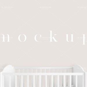 May include: A white crib with a white slatted headboard and footboard against a light beige wall. The word "mockup" is written in white letters on the wall.