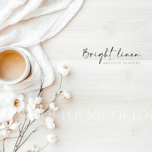 May include: A flat lay composition with a white mug containing a light brown drink, placed on white linen. White flowers and the text "Bright linen ARTISTIC FLATLAY" are arranged on a light wood surface, creating a minimalist aesthetic.