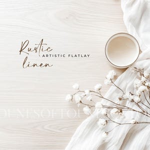 Puede incluir: Una tela de lino blanca con una taza de cerámica blanca y una rama de flores blancas. El texto "Rustic linen Artistic Flatlay" está escrito en marrón sobre un fondo de madera blanca.