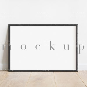 May include: A black picture frame with a white mat and a white background. The frame is sitting on a light wood floor.