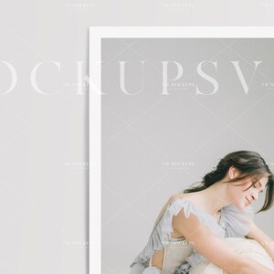 May include: A woman in a light blue dress with ruffles sits on a white surface. The background is a light gray wall.