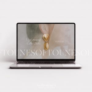 Może przedstawiać: Laptop wyświetla reklamę biżuterii. Na ekranie widnieje złoty kolczyk z g&oacute;rą w kształcie serca i dołem w kształcie łzy. Tekst na ekranie brzmi "Upcoming Collection" i "02.05.2025". Laptop jest srebrny i stoi na białej powierzchni.