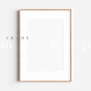 Puede incluir: Maqueta de marco de fotos rectangular con un passe-partout blanco y un marco de color madera clara. El marco está centrado sobre un fondo blanco. Las palabras "FRAME mockup" están impresas en color claro.