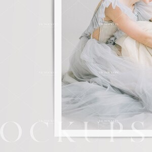 May include: A woman wearing a light blue tulle dress with a ruffled neckline. The dress is flowing and ethereal, and the woman is sitting on a white surface.