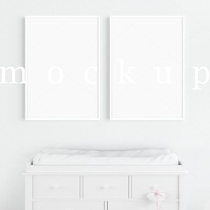 May include: Two white picture frames with white mounts hanging on a white wall above a white changing table with a white changing mat.