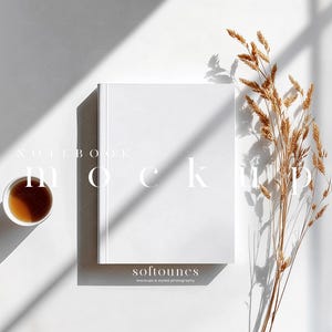 Puede incluir: Maqueta de cuaderno blanco con la palabra «mockup» impresa en la portada. Una taza de té y tallos de trigo secos se colocan sobre una superficie blanca. También se ve el texto «softounes mockups & styled photography».