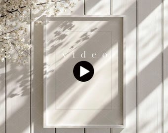 May include: A white framed video mockup with the word "video" in a light font. A black play button is in the center. The frame is against a white wooden background with shadows and a floral branch.