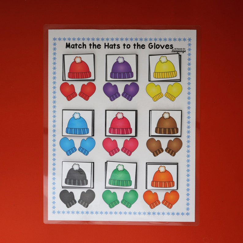 Puede incluir: Un juego educativo laminado con el texto "Match the Hats to the Gloves". El juego presenta ilustraciones coloridas de gorros y guantes en varios colores, incluyendo rojo, morado, amarillo, azul, rosa, marr&oacute;n, gris, verde y naranja. El borde est&aacute; decorado con copos de nieve azules.