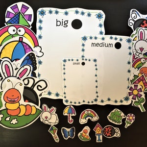 May include: A set of colorful felt cutouts featuring various shapes, animals, and objects, including a butterfly, a rainbow, a ladybug, a caterpillar, a frog, a flower, a house, an umbrella, a kite, and a bunny. The cutouts are arranged on a black background with three white cards labeled "big", "medium", and "small".