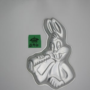 Może przedstawiać: Srebrna metalowa forma do ciasta w kształcie Bugs Bunny'a trzymającego marchewkę. Forma jest przeznaczona do pieczenia ciasta w kształcie Bugs Bunny'a.
