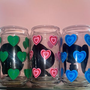 May include: Three clear glass cups with black silhouettes and colorful heart designs. The cups have green, pink, and blue hearts.