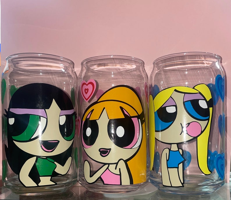 May include: Three clear glass jars with colorful cartoon images of the Powerpuff Girls. The jars are decorated with pink hearts and blue swirls. The characters are Bubbles, Buttercup, and Blossom.