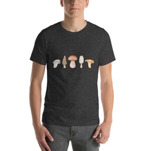 Może przedstawiać: Szary t-shirt w ciemnym melanżu z nadrukiem pięciu r&oacute;żnych rodzaj&oacute;w grzyb&oacute;w na przodzie. Grzyby są w odcieniach brązu, bieli i ż&oacute;łci.