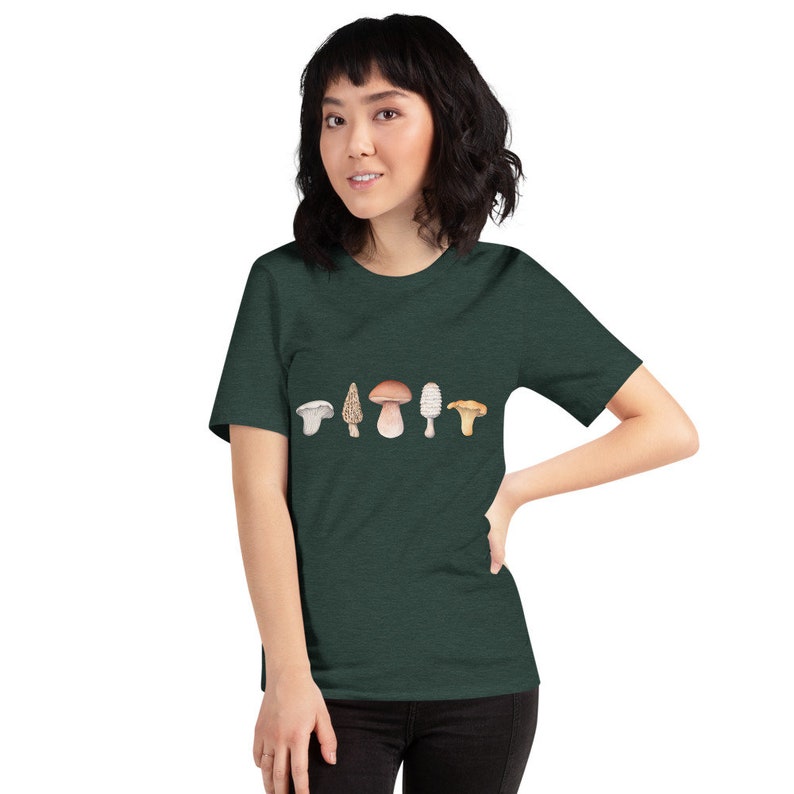 Może przedstawiać: Zielony t-shirt z nadrukiem pięciu r&oacute;żnych rodzaj&oacute;w grzyb&oacute;w na przodzie. Grzyby są w odcieniach brązu, bieli i ż&oacute;łci.