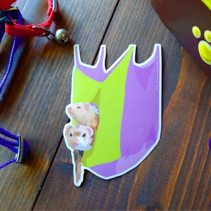 May include: A sticker showing two ferrets emerging from a purple and green shape. The sticker has the text "The Roaming Ferret" on the side. A purple and red pet collar and a brown pet carrier are also visible.