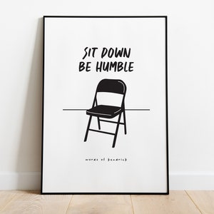 May include: Black and white print with the text "Sit down be humble" and a black folding chair. The text "words of remarkable" is at the bottom of the print.