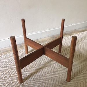 May include: A wooden plant stand with four legs and a cross-shaped design. The stand is made of natural wood and has a rustic look.