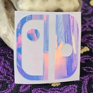 May include: A holographic sticker featuring the Nintendo Switch logo in a white outline against a purple, pink, and blue background.