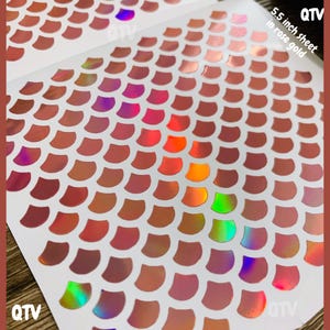 May include: A 5.5 inch sheet of rose gold metallic stickers featuring a repeating pattern of individual fish scale shapes. The stickers have a reflective, iridescent finish that shifts between copper, pink, and green hues under the light.