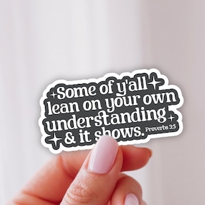 May include: A dark gray die-cut sticker with a white border featuring the white text Some of y'all lean on your own understanding & it shows. Proverbs 3:5, accented with small four-pointed star icons in a retro-inspired typography style.