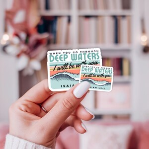 May include: Two stickers with the text "WHEN YOU GO THROUGH DEEP WATERS I will be with you". The stickers have a design of waves and a colorful sunset. The smaller sticker has the text "AIAH 43:2".