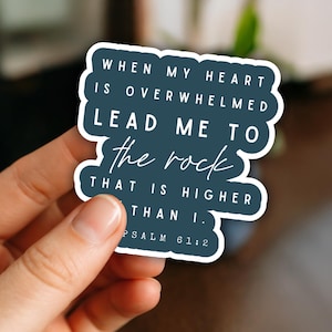 May include: A dark blue die-cut sticker with a white border featuring the white text: WHEN MY HEART IS OVERWHELMED LEAD ME TO the rock THAT IS HIGHER THAN I. PSALM 61:2. The sticker has a matte finish and a scalloped, irregular shape.