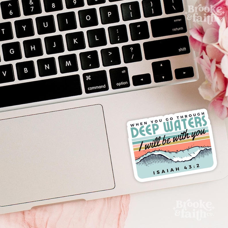 May include: A rectangular sticker on a laptop featuring the text "WHEN YOU GO THROUGH DEEP WATERS I will be with you" with a wave and mountain design. The sticker has a light blue, orange, and teal color scheme. The text "ISAIAH 43:2" is also included.