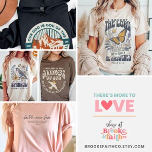 May include: A collection of five t-shirts with different Christian-themed designs. The designs include mountains, a sparrow, a dove, a butterfly, and a heart. The text on the shirts includes "Our God is God of the Mountains", "His eye is on the sparrow", "I will sing of the goodness of God", "I sought the Lord and he heard and he answered", and "There's more to love".