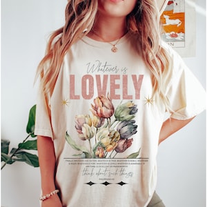 May include: A cream colored t-shirt with a pink floral design and the text "Whatever is LOVELY" in pink. The text "Finally brothers and sisters, whatever is true, whatever is noble, whatever is right, whatever is pure, whatever is lovely, whatever is admirable - if anything is excellent or praiseworthy think about such things. Philippians 4:8" is printed in black below the floral design.