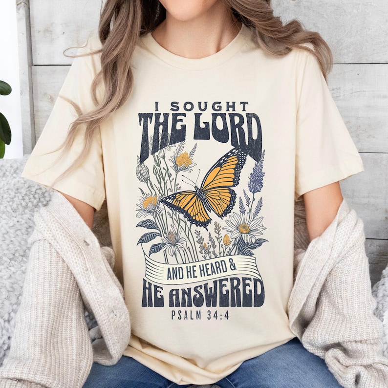 May include: A beige t-shirt with a butterfly and floral design. The text on the shirt reads "I sought the Lord and he heard & he answered Psalm 34:4".