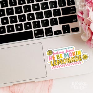 Może przedstawiać: Kolorowa naklejka z napisem "LIFE GAVE ME SOME LEMONS but my Jesus HE BE MAKIN' LEMONADE" umieszczona na laptopie. Naklejka zawiera grafikę cytryny oraz r&oacute;żowo-ż&oacute;łty wz&oacute;r w szachownicę.