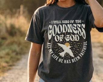 Puede incluir: Una camiseta de manga corta gris carbón con un estampado gráfico que incluye el texto I WILL SING OF THE GOODNESS OF GOD y ALL MY LIFE HE HAS BEEN FAITHFUL, rodeando una ilustración central de un pájaro volando frente a un sol.