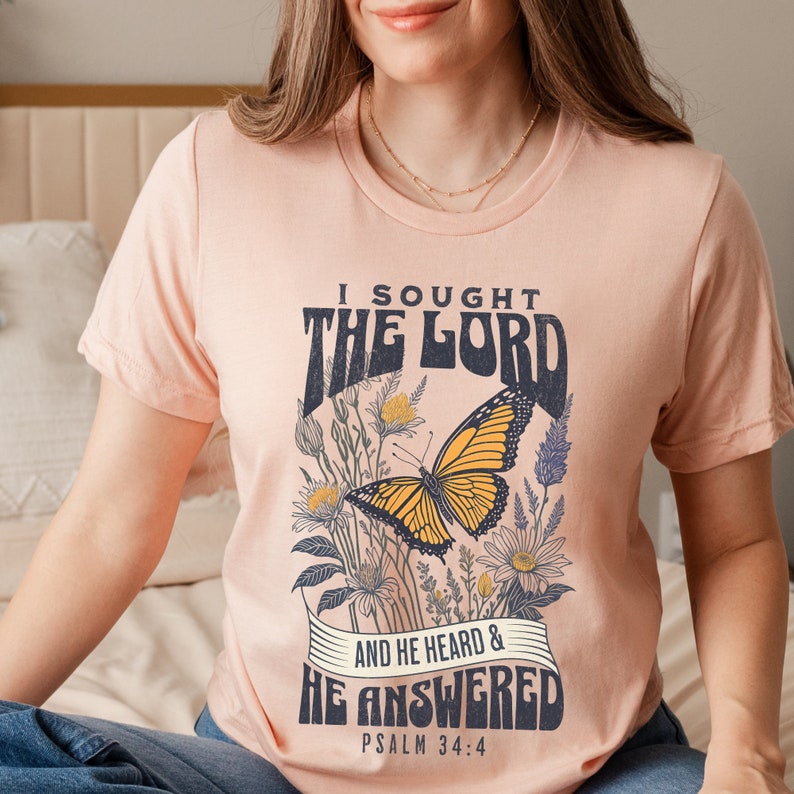May include: A peach-colored t-shirt with a butterfly graphic and the text "I sought the Lord and he heard & he answered Psalm 34:4".