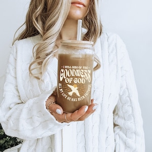 May include: A clear glass tumbler with a bamboo lid and a straw. The tumbler has a graphic design with the text "I will sing of the Goodness of God. All my life He has been faithful."