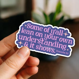May include: A sticker with the text "Some of y'all lean on your own understanding & it shows. Proverbs 3:5" in pink and white on a purple background. The sticker is held by a hand.