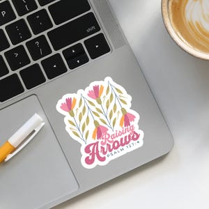 May include: A sticker with a floral design and the text "Raising Arrows" with the Bible verse "Psalm 127:4" underneath.