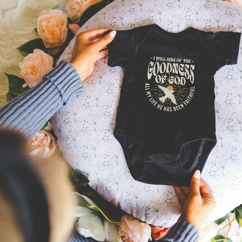 May include: Black baby onesie with a white graphic design featuring a dove and the text "I will sing of the goodness of God, all my life he has been faithful".