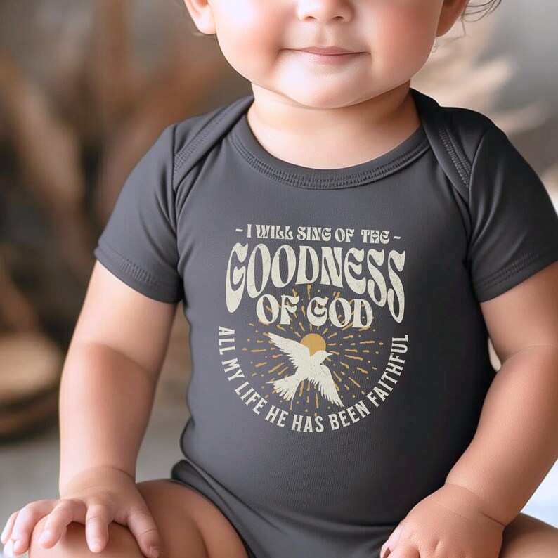 May include: A dark grey baby onesie with a white graphic design featuring a bird and the text "I will sing of the goodness of God all my life he has been faithful".