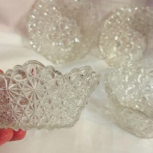 May include: A set of three clear pressed glass bowls featuring a repeating starburst and hobnail pattern. Each bowl has a scalloped rim and a textured exterior surface. The glass is transparent and reflects light across its intricate geometric design.
