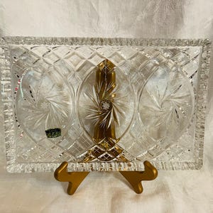 May include: A rectangular clear glass serving tray featuring a decorative diamond-cut pattern along the border and three circular sections with etched starburst designs. A small green and gold sticker is visible on the left side of the glass.