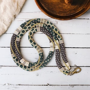 以下が含まれることがあります： 金、緑、茶色の模様が施された長いビーズネックレス。ネックレスには金属製の留め具が付いています。