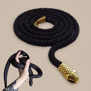 Op de afbeelding: Een zwarte kralen slangenketting met een gouden slangenkoppen sluiting. De ketting is opgerold en de kop is gericht op de camera.