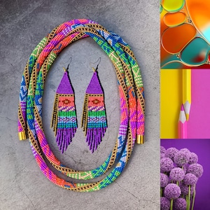 Puede incluir: Un collar de cuentas de colores con un patrón geométrico en tonos de rosa, azul, verde y dorado. El collar se combina con pendientes a juego con un diseño de flecos en morado y rosa.