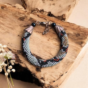 Peut inclure: Un bracelet en perles avec un motif géométrique dans les tons de noir, gris et blanc. Le bracelet a des embouts de couleur cuivre et un fermoir argenté.