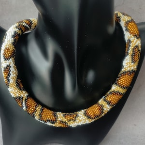 May include: A beaded necklace with a brown, white and black snake skin pattern.