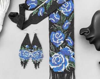 May include: A black beaded necklace with blue and white floral embroidery and black fringe. Matching earrings with blue and white floral embroidery and black fringe.