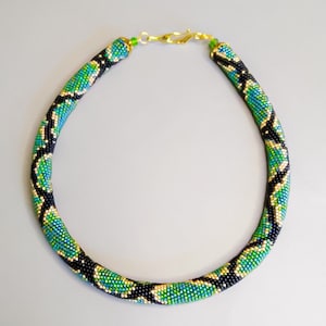 Pode incluir: Um colar de contas com um padrão de pele de cobra preto, verde e dourado. O colar é feito de contas pequenas e tem um fecho dourado.