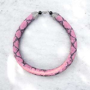 May include: A pink and black beaded necklace with a snakeskin pattern. The choker-style necklace has silver-toned metal end caps and a clasp. The beads form a tubular shape.