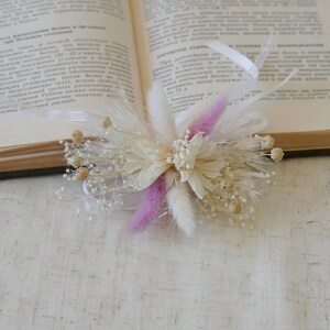 May include: A small bouquet of dried flowers with white and pink pampas grass, white baby's breath, and white dried flowers.