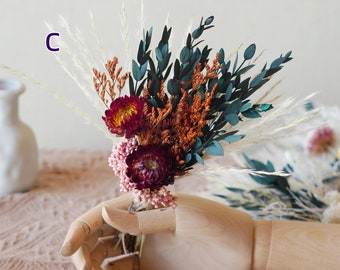 May include: A bouquet of dried flowers in a wooden hand. The bouquet includes burgundy, pink, and orange flowers, as well as green and white dried grasses.